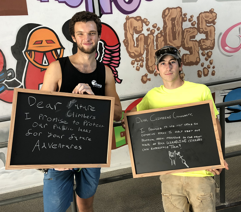 Two individuals holding chalkboards with messages about protecting public lands and the climbing community.