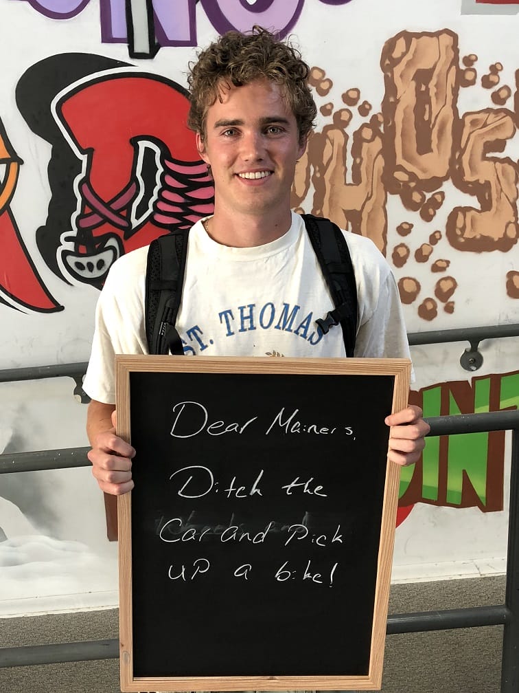 Person holding a chalkboard sign with handwritten message, standing in front of colorful graffiti wall.