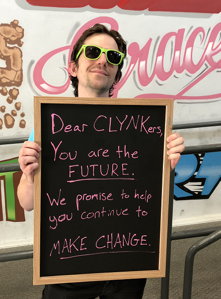 Person in sunglasses holds a chalkboard sign with a positive message about making change.