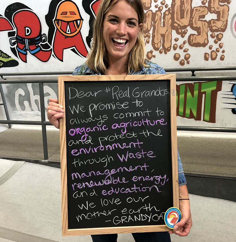 Person holding a chalkboard with a message about commitment to organic agriculture, waste management, and renewable energy