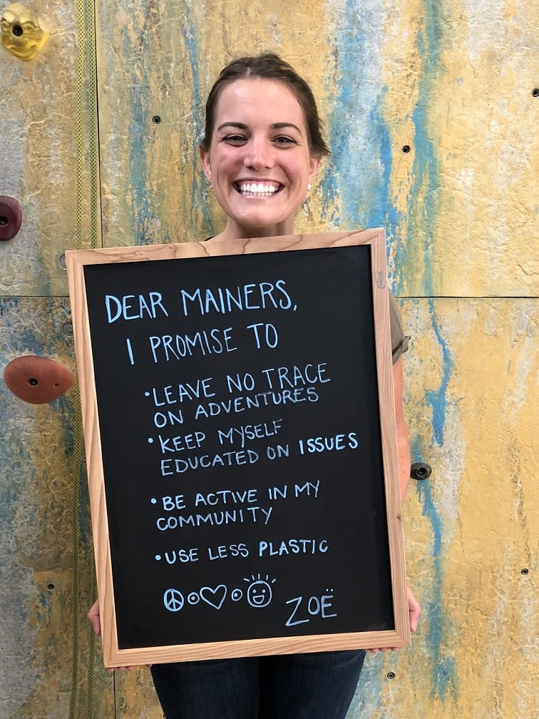 Smiling woman holding a chalkboard pledging eco-friendly actions like reducing plastic and being active in the community.