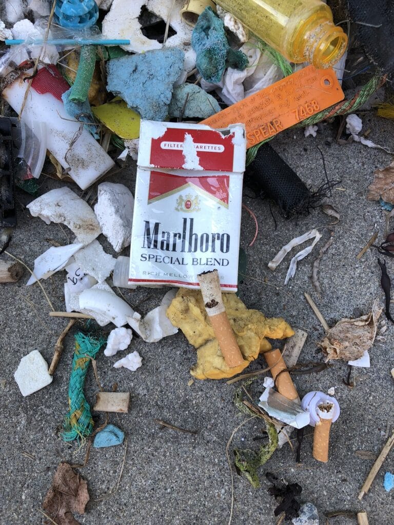 Cigarette pack and butts littered on the ground amidst scattered trash and debris.