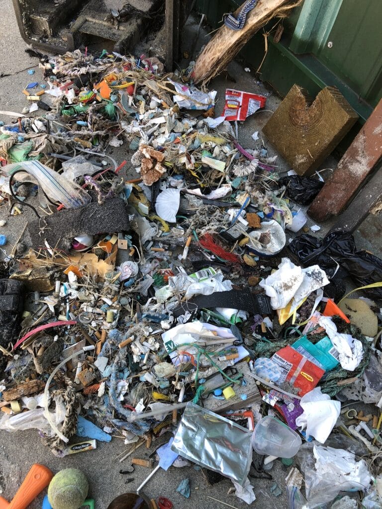 Pile of assorted trash and debris on the ground near a building wall.