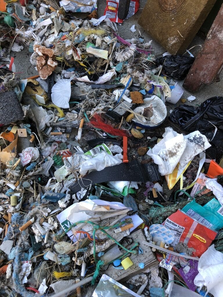 Pile of assorted trash and debris including plastic, paper, and cigarette butts on the ground.