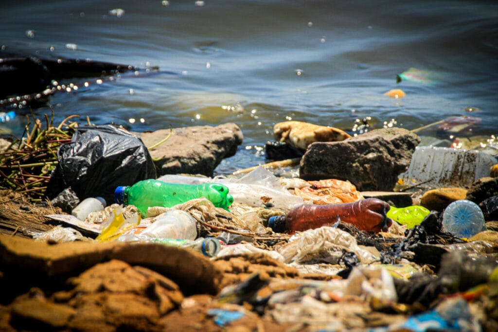 Plastic and trash pollution on a riverbank with water in the background.