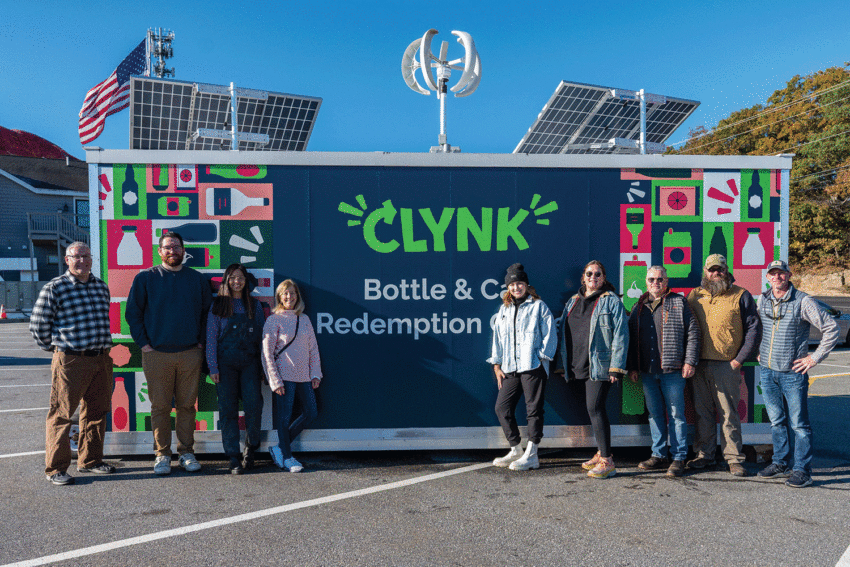 Nine people standing in front of a Clynk bottle and can redemption kiosk with bright artwork and solar panels.