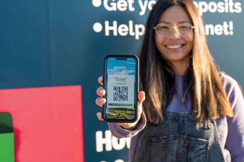 Smiling woman holds smartphone displaying a QR code against a background with environmental messages.