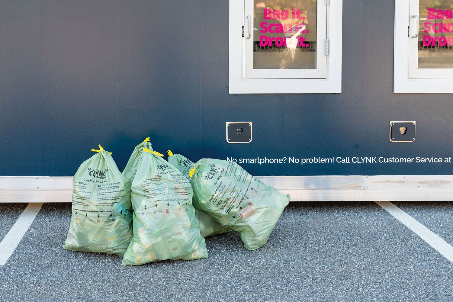 Recycling bags filled outside a CLYNK location against a wall with promotional text and contact information.