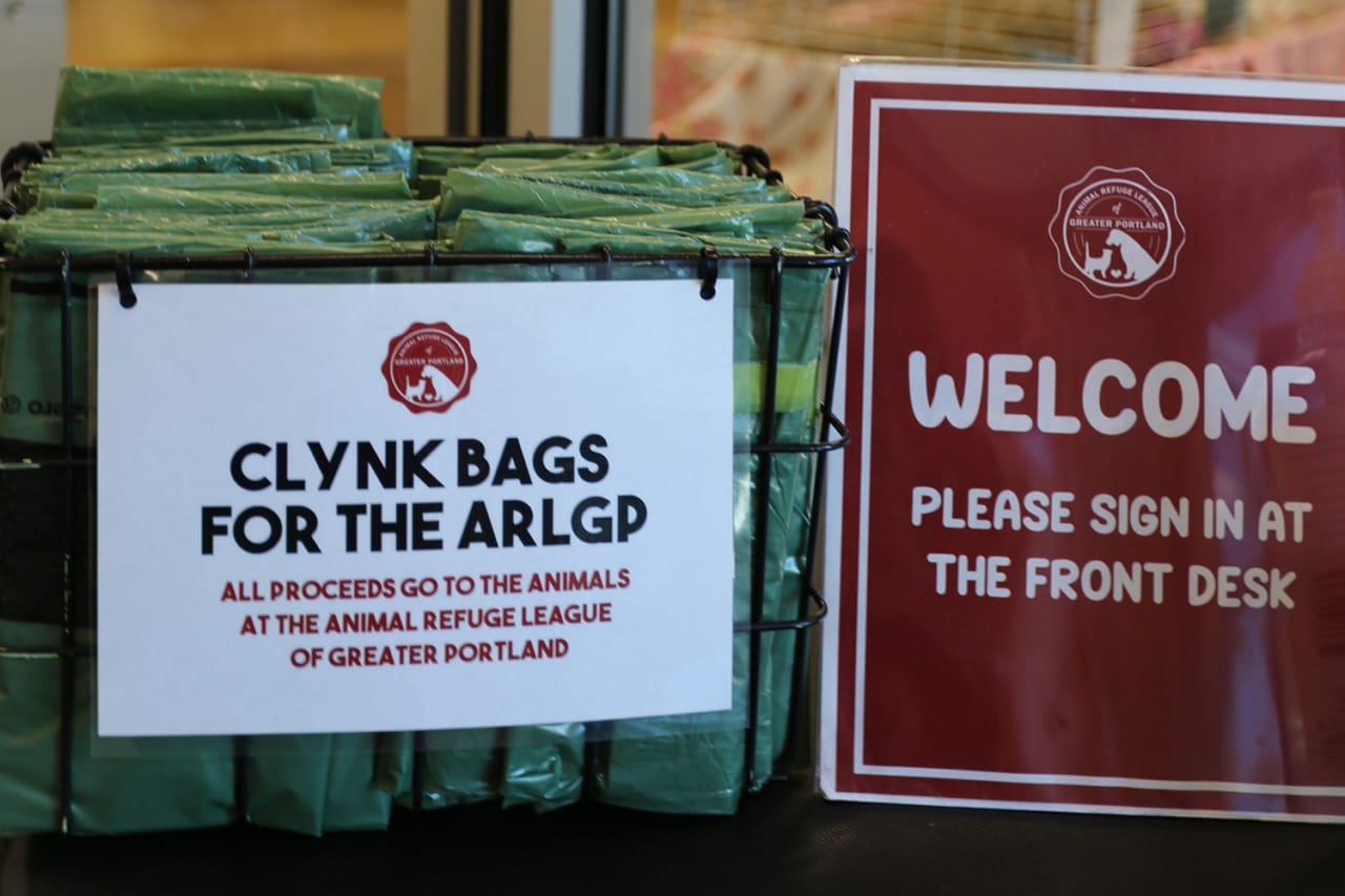 Basket with Clynk bags for ARLGP donations next to a welcome sign asking visitors to sign in at the front desk.