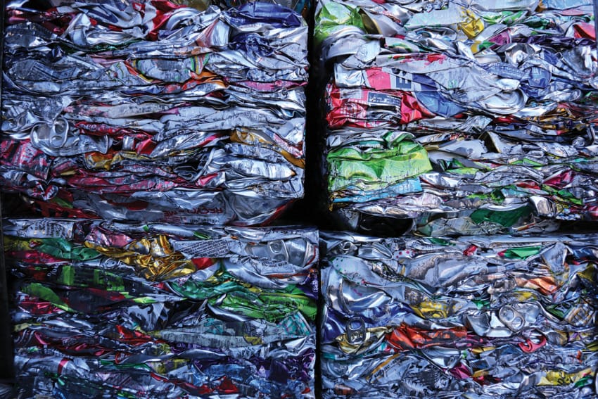 Stacked, crushed aluminum cans in a recycling facility, showcasing vibrant colors and textures of compacted metal.