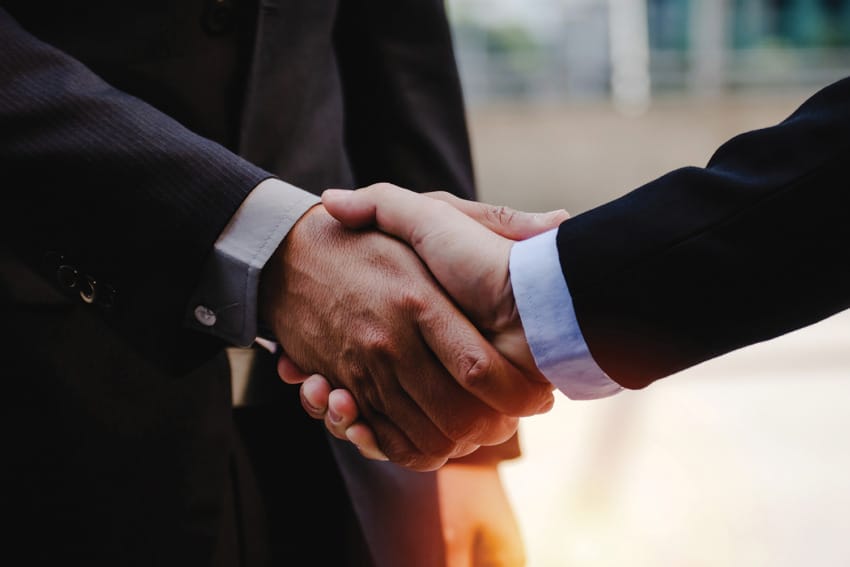 Two people in business attire shaking hands, symbolizing agreement or partnership.