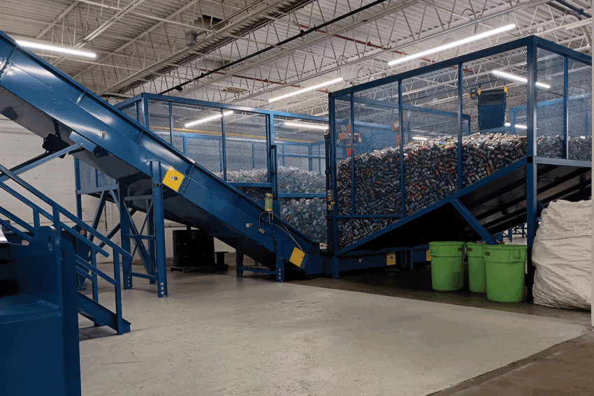 Conveyor belt system sorting plastic bottles in an industrial recycling facility with large containers and high ceiling.