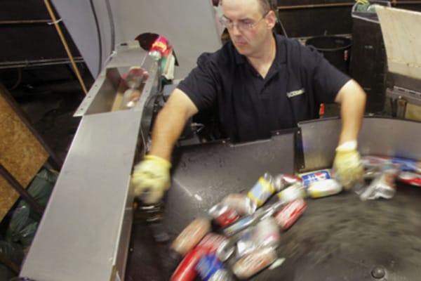 Man sorting aluminum cans on a recycling conveyor belt in an industrial facility.